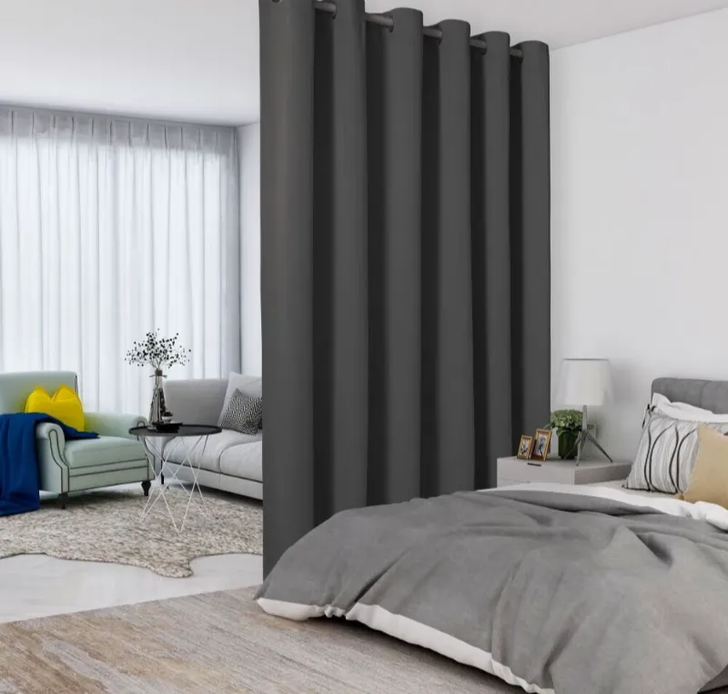 Dark gray noise reduction curtains hanging in a modern bedroom setting with a bed and sofa.