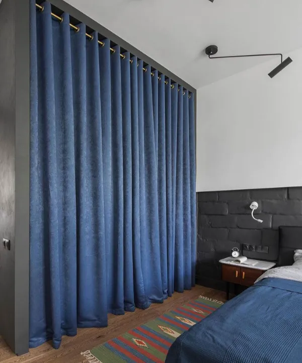 Blue soundproof curtains installed in a room with a bed and side table.